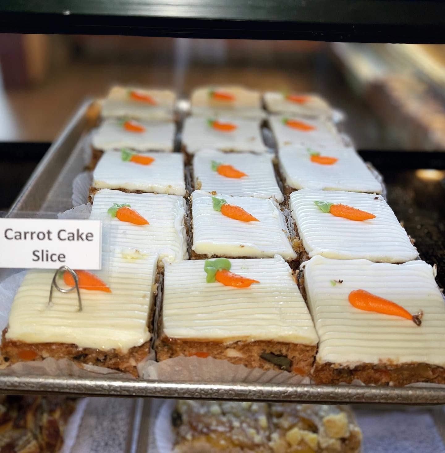 Tray of carrot cake slices with cream cheese frosting and fondant carrot decorations